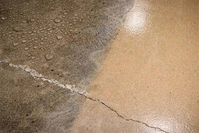 Water beading on a coated floor next to cracked bare concrete
