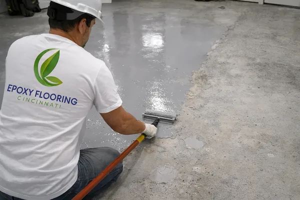 Installer in an Epoxy Flooring Cincinnati shirt rolling a gray base coat over a patched slab